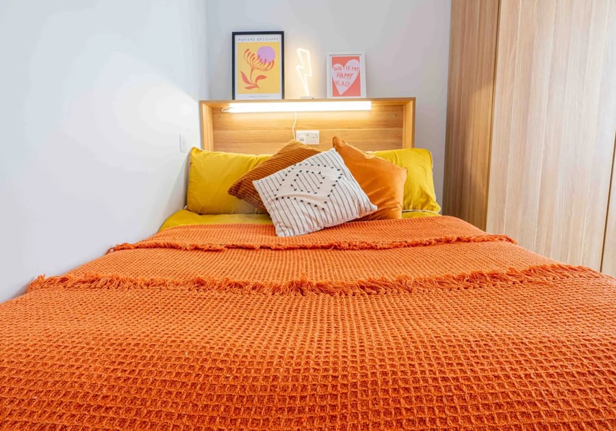Bed with orange throw pillows artwork and wardrobe bedroom at iQ Sterling Court in London Student Accommodation