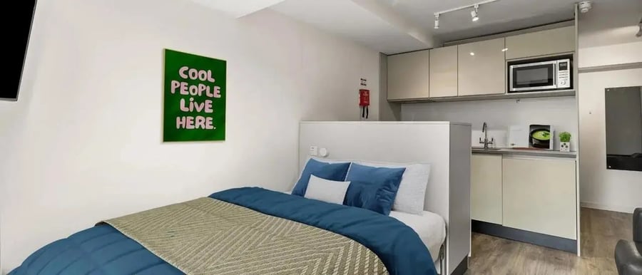 Bed with blue bedding and kitchen area bedroom at Chapter Islington in London Student Accommodation