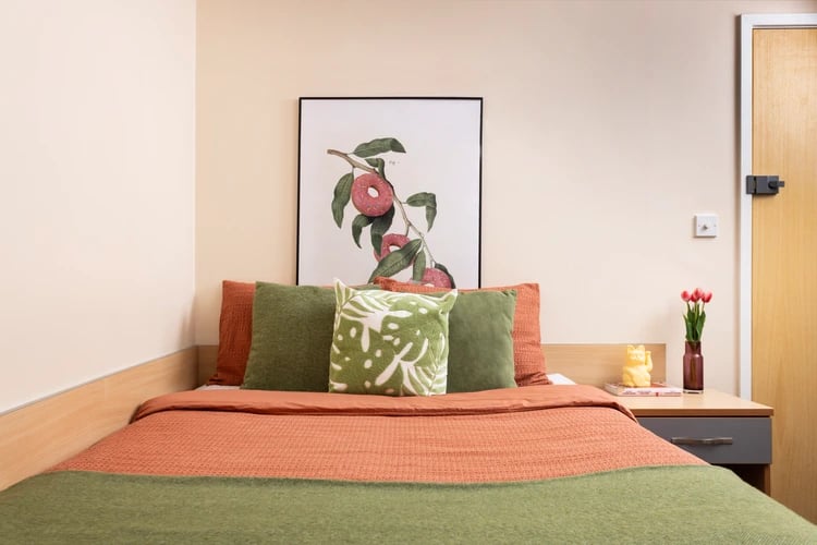 Bed with orange and green blankets and art bedroom at Lennon Studios in Liverpool Student Accommodation