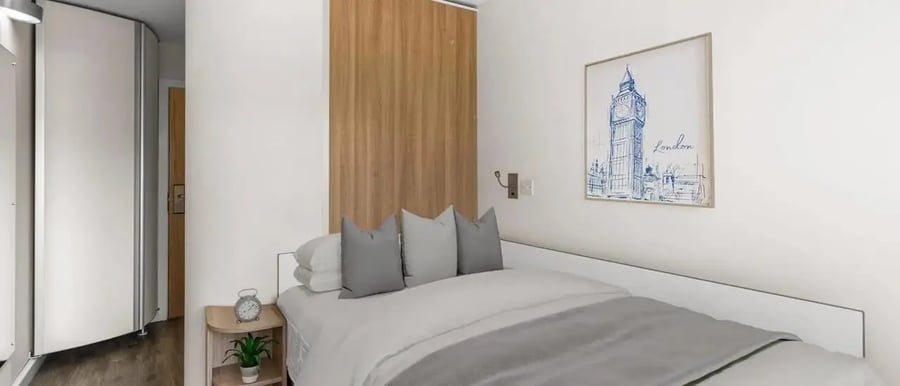 Bed with pillows alarm clock and London painting bedroom at Chapter Islington in London Student Accommodation