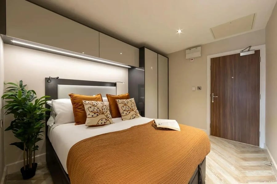 Bed with orange throw pillows and plant bedroom at dwell 121 Princess Street in Manchester Student Accommodation