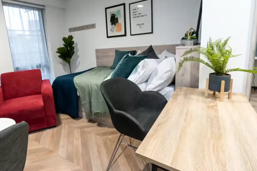 Bed with green blankets red armchair study area at Steelworks in Sheffield Student Accommodation