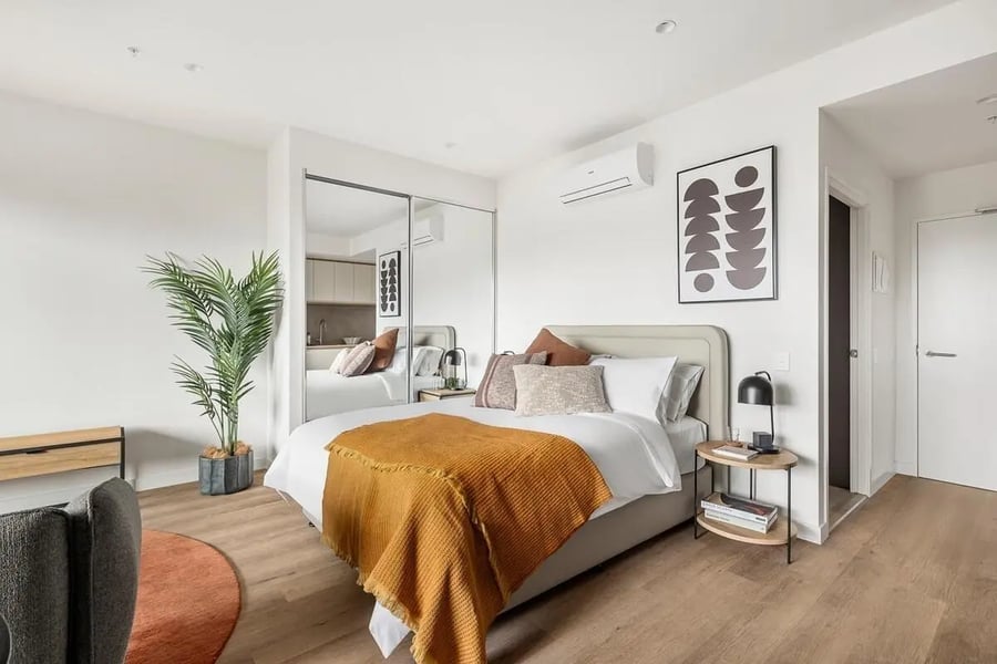 Bed with orange throw mirrored closet plant bedroom at Caulfield Place in Melbourne Student Accommodation