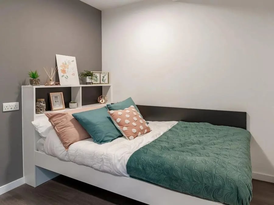 Bed with pillows shelf art and green bedding bedroom at Pavilion Court London in London Student Accommodation