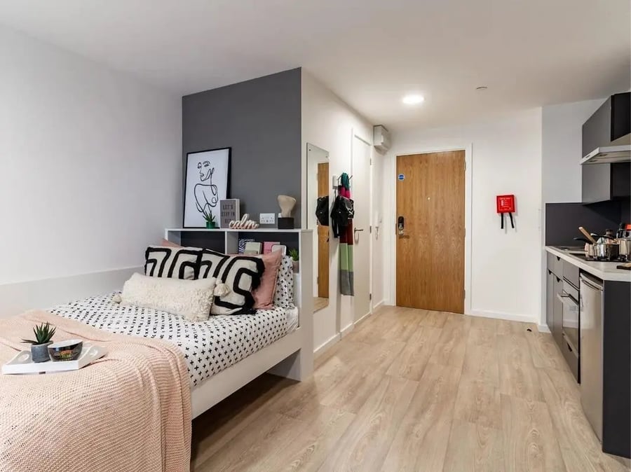 Bed with pillows blanket shelf artwork and kitchen studio apartment at Pavilion Court London in London Student Accommodation