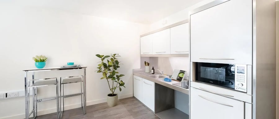 Bar stools with table, plant, and microwave kitchen at Chapter Spitalfields in London Student Accommodation