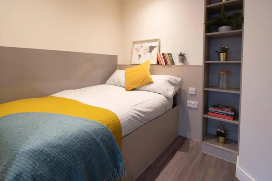 Bed with yellow pillow and throws shelving unit bedroom at Redvers Tower in Sheffield Student Accommodation