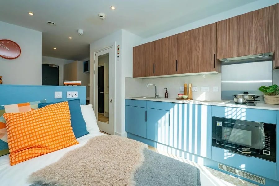 Bed with orange pillows and blue kitchen studio apartment at The Propeller Quarter in Bristol Student Accommodation