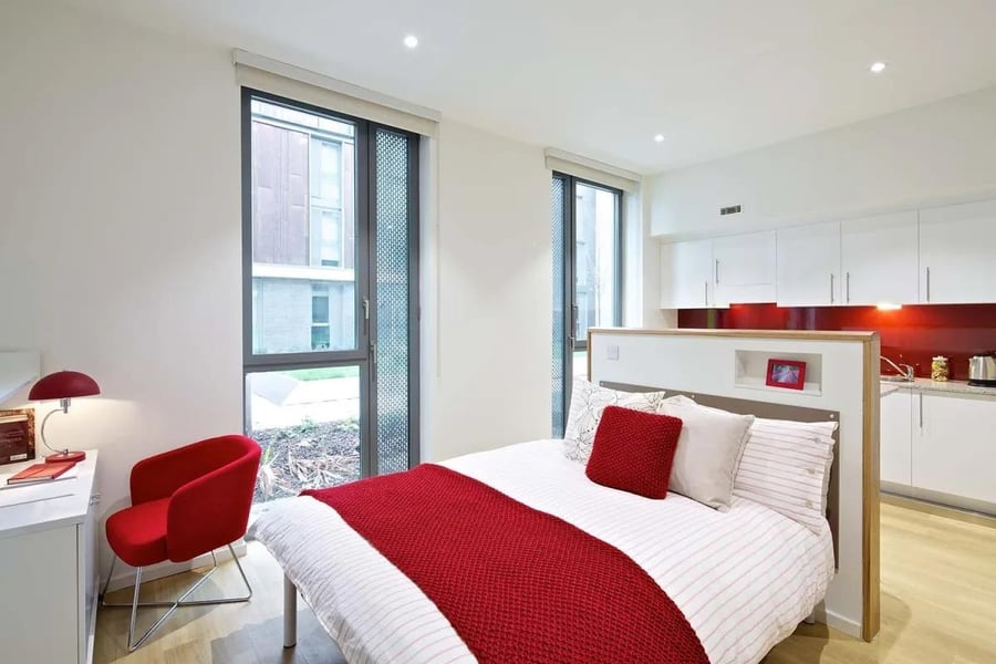 Bed desk red chair and kitchen area studio. at Wood Lane Studios in London Student Accommodation