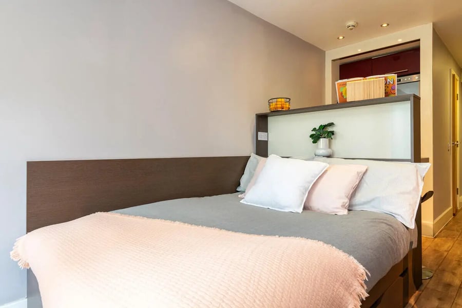 Bed with pillows and blanket kitchen area bedroom at Collegiate Dashwood Studios in London Student Accommodation