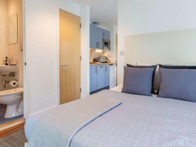 Bed with kitchen and bathroom visible bedroom at Harbour Court in Bristol Student Accommodation