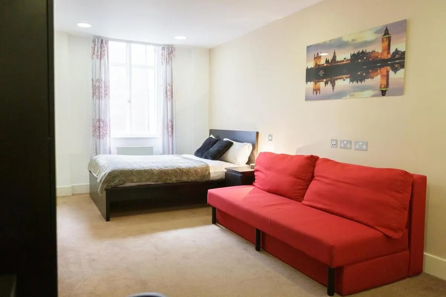 Bed with red sofa and London artwork Living room at AXO Oxford Circus in London Student Accommodation