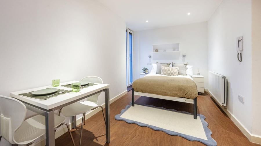 Table chairs bed rug and bedside cabinet bedroom at Griffon Studios in London Student Accommodation