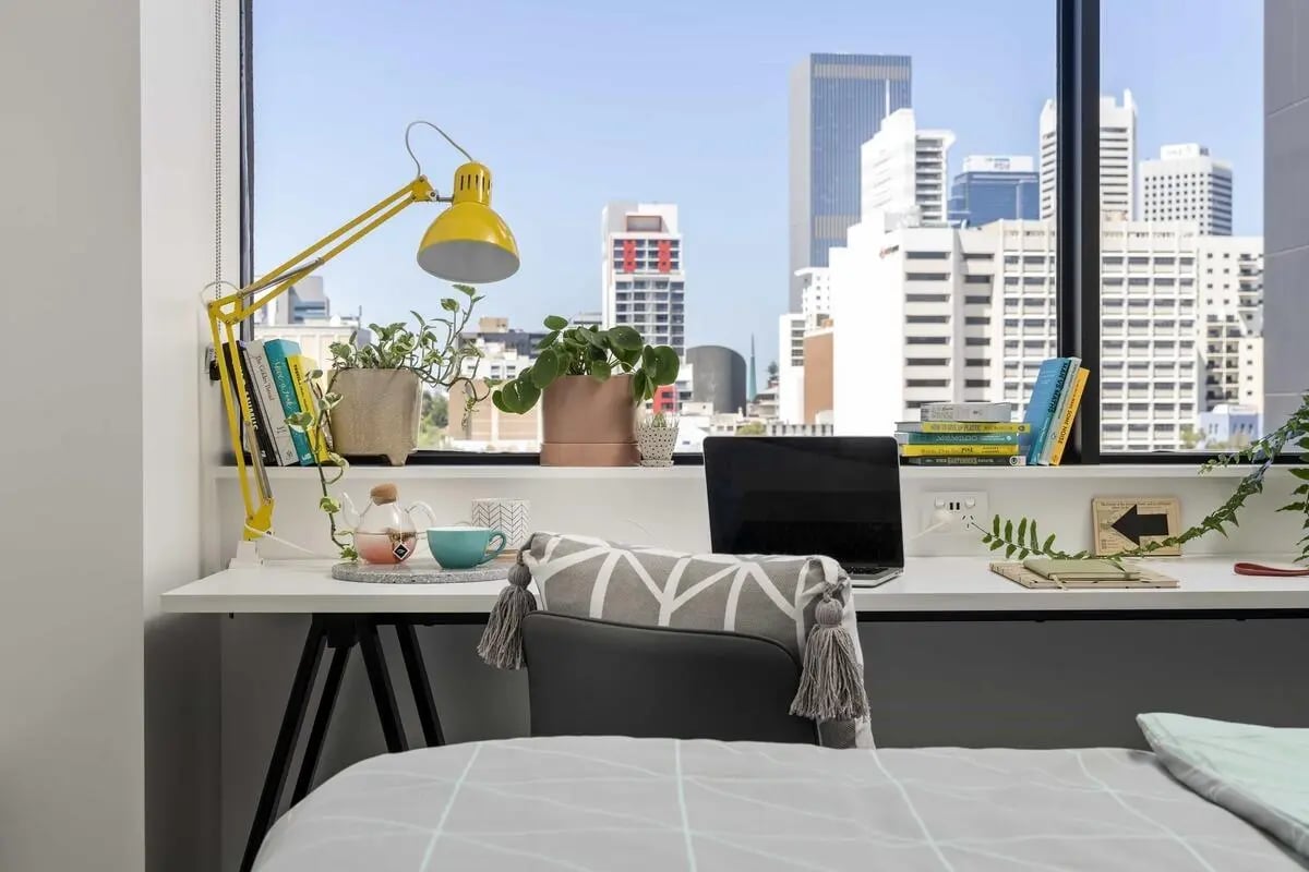 Desk with lamp laptop books plants and city view study area at Campus Perth in Perth Student Accommodation