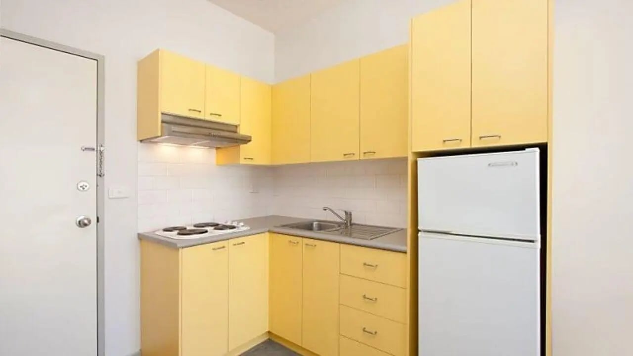 Yellow cabinets white tiled backsplash stovetop sink refrigerator kitchen at Student Living - 570 Swanston in Melbourne Student Accommodation