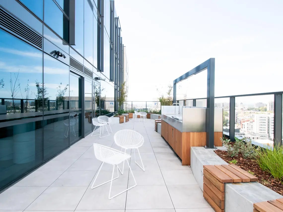 Outdoor kitchen with white chairs and cityscape view exterior at Yugo Berkeley Street in Melbourne Student Accommodation