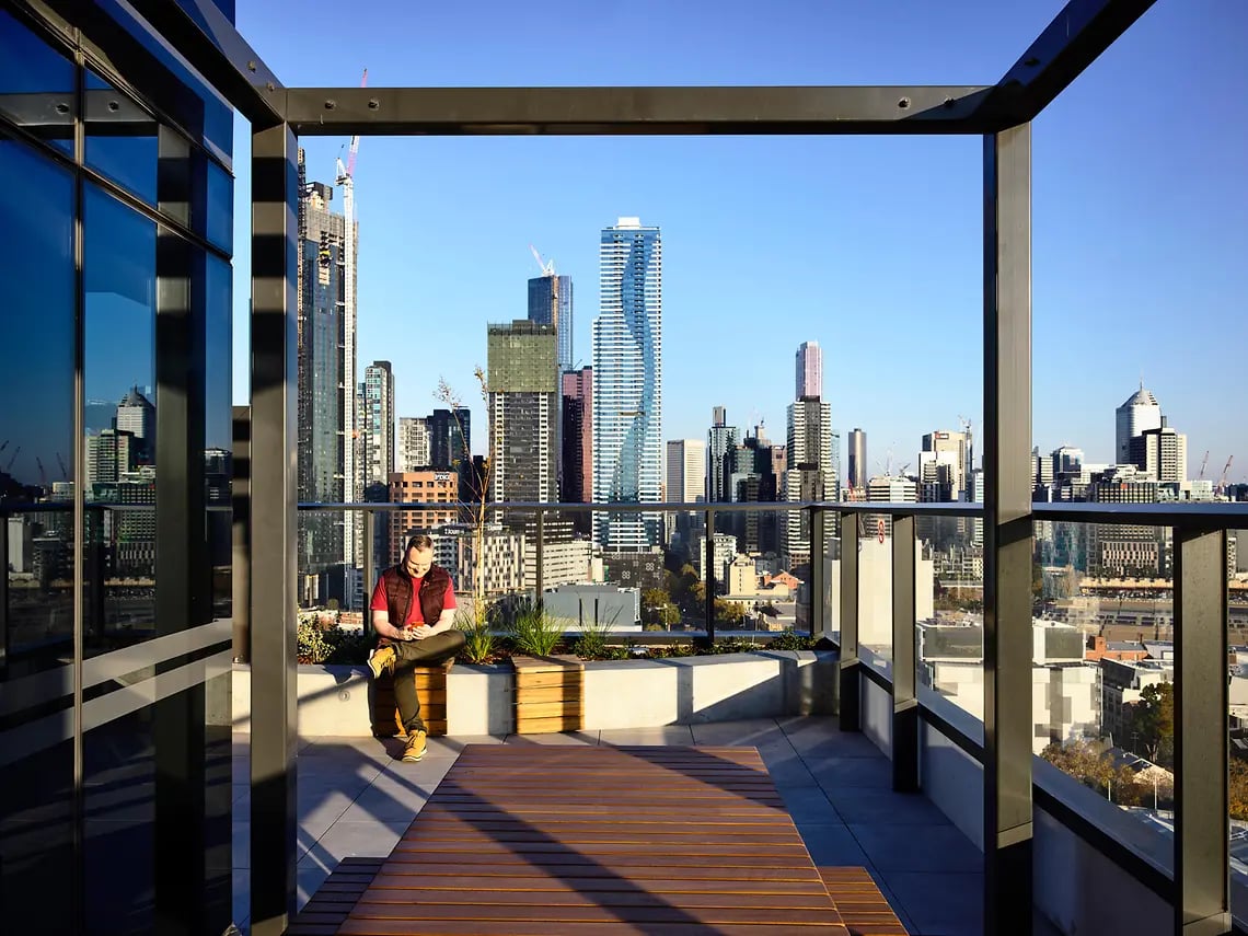 Man on bench with city skyline outdoor area exterior at Yugo Berkeley Street in Melbourne Student Accommodation