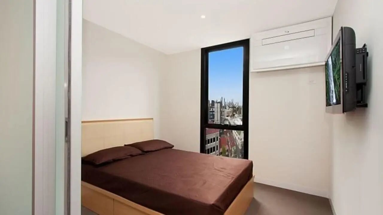 Bed with brown sheets air conditioner wall mounted television bedroom at Student Living on Villiers in Melbourne Student Accommodation