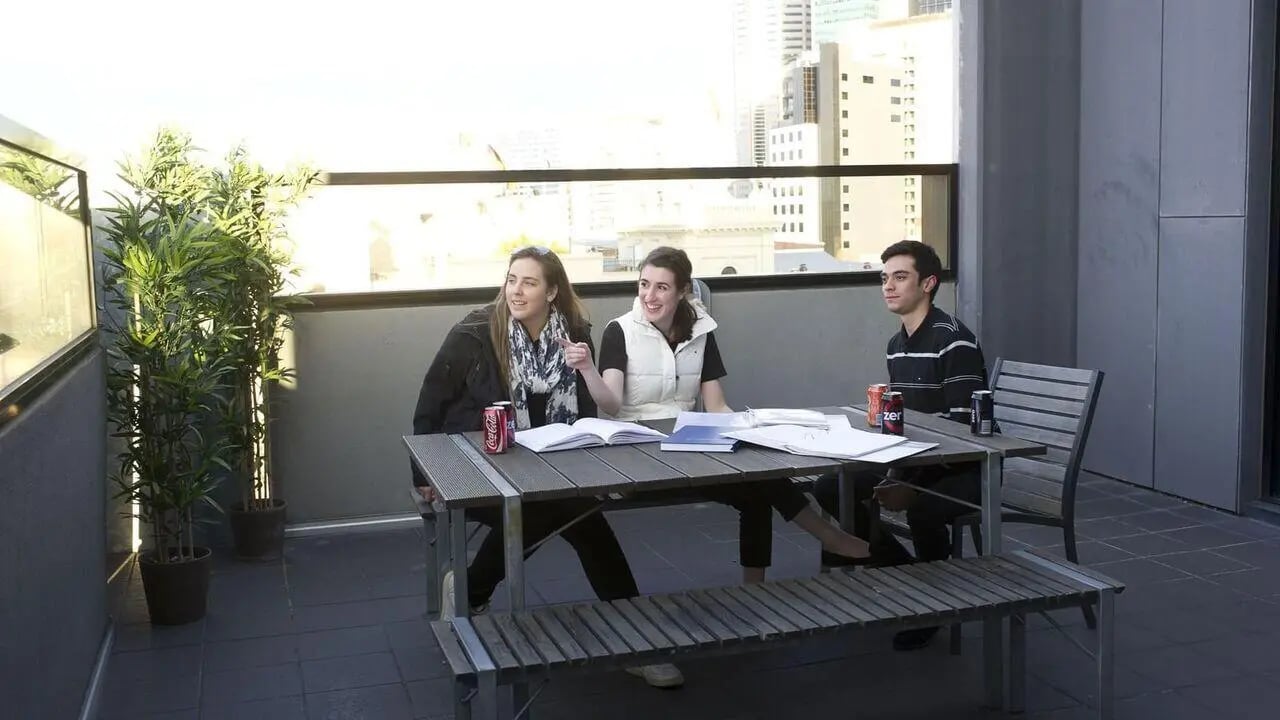 Students sit at table with books and drinks balcony exterior at Student Living On Campus in Melbourne Student Accommodation