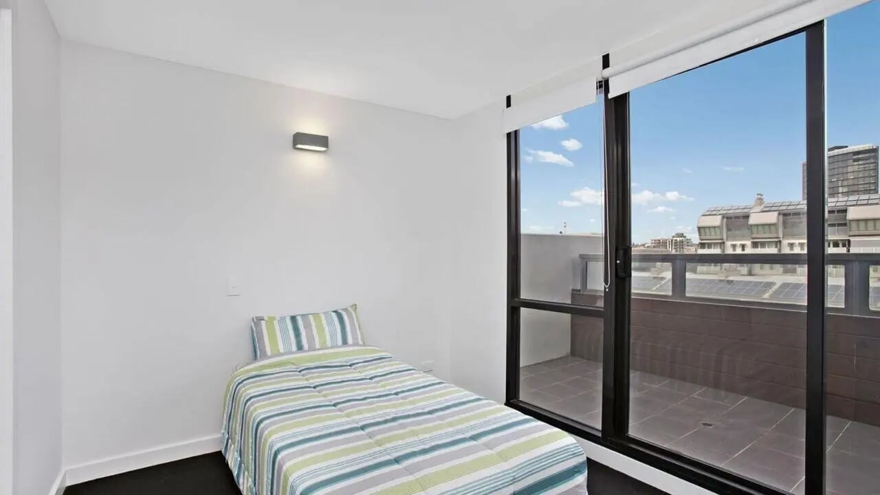 Bed with striped comforter balcony view bedroom at Student Living on Raleigh in Melbourne Student Accommodation