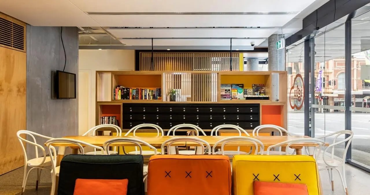 Table chairs mailboxes luggage colorful lounge area at Iglu Central in Sydney Student Accommodation