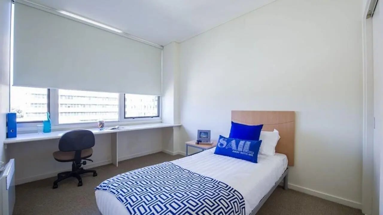 Bed desk chair with blue pillows bedroom at Student Living-590 Lygon in Melbourne Student Accommodation