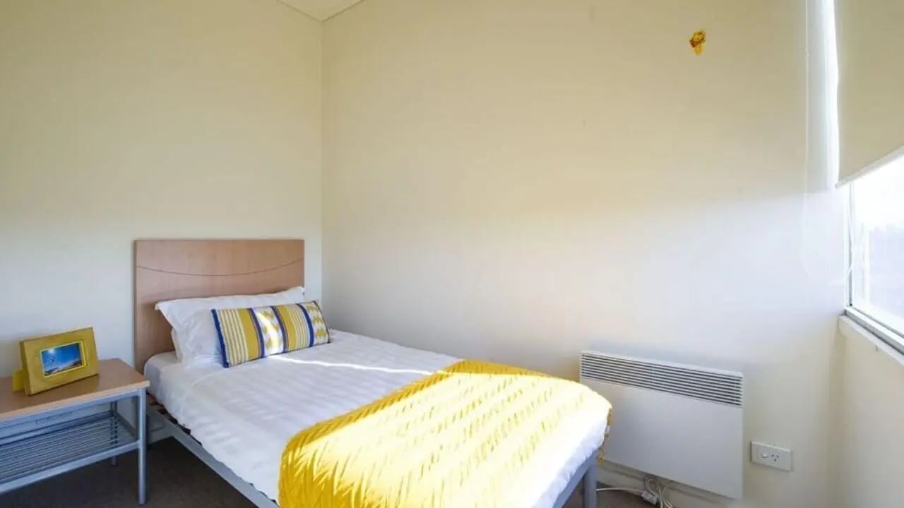 Bed with yellow throw and bedside table bedroom at Student Living - 570 Lygon in Melbourne Student Accommodation