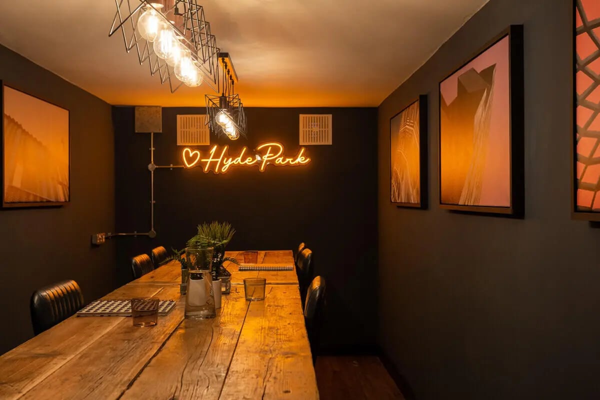 Long wooden table, chairs, neon sign, art. Dining area. at Hyde Park in Leeds Student Accommodation