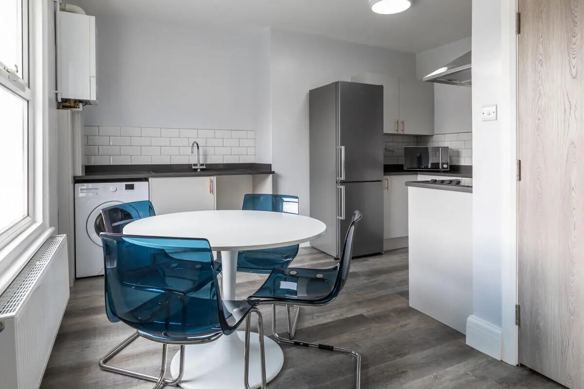 Round table blue chairs fridge washing machine kitchen at Hyde Park in Leeds Student Accommodation