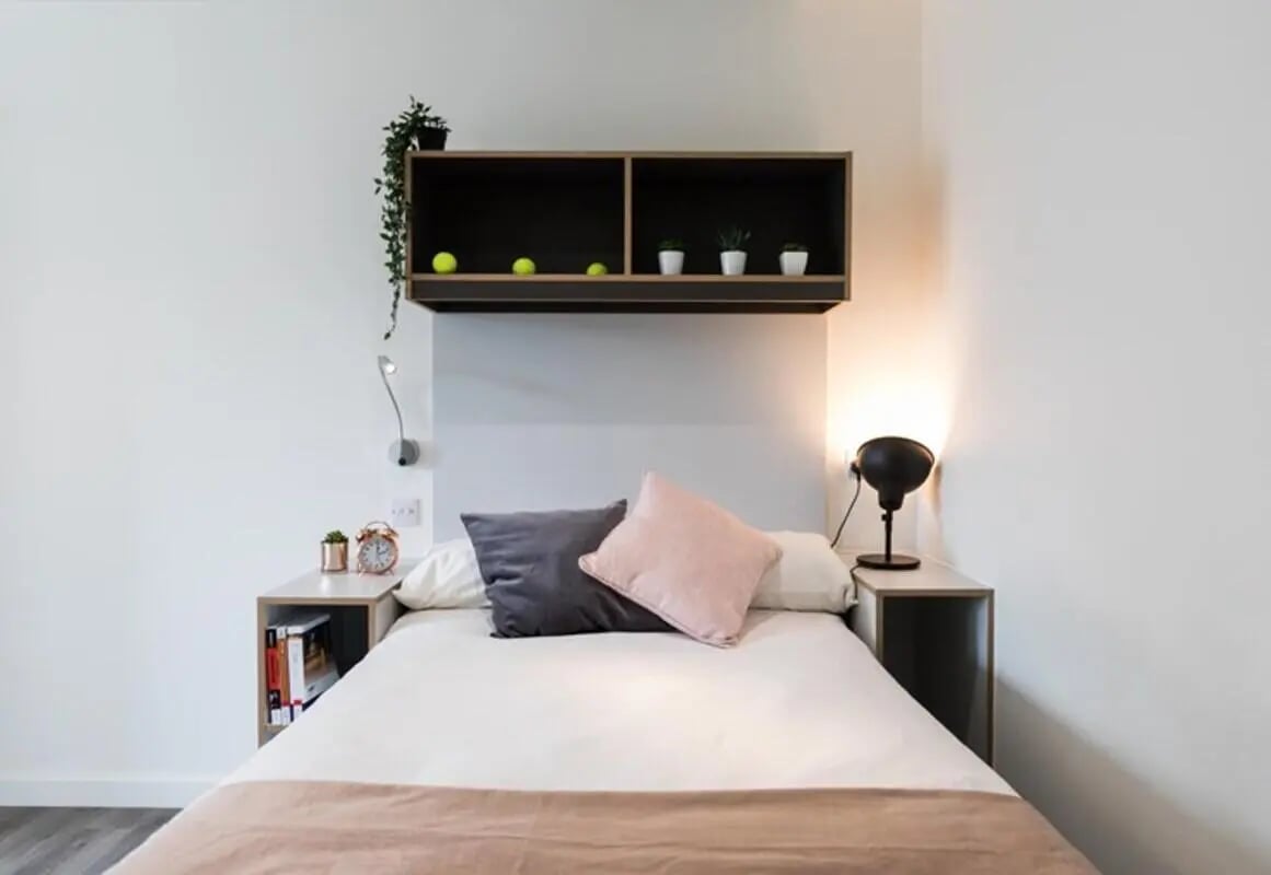 Bed pillows lamp clock shelf with plants bedroom at The Cam Foundry in Cambridge Student Accommodation
