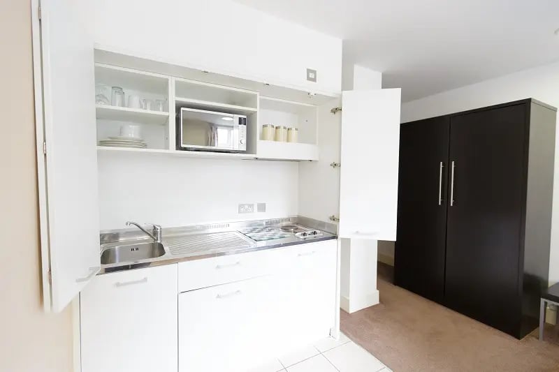 White cabinets microwave sink and dark wardrobe kitchen at AXO Oxford Circus in London Student Accommodation