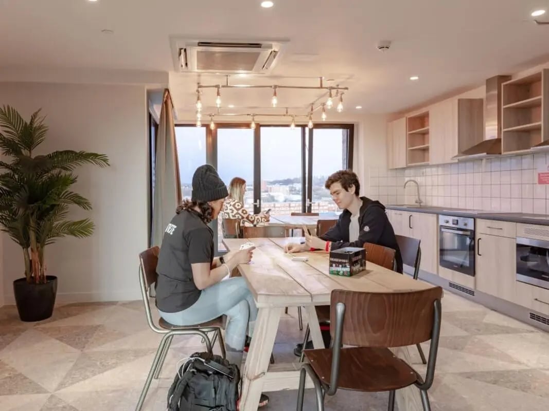 Students playing cards at wooden table communal kitchen living room at True Glasgow in Glasgow Student Accommodation