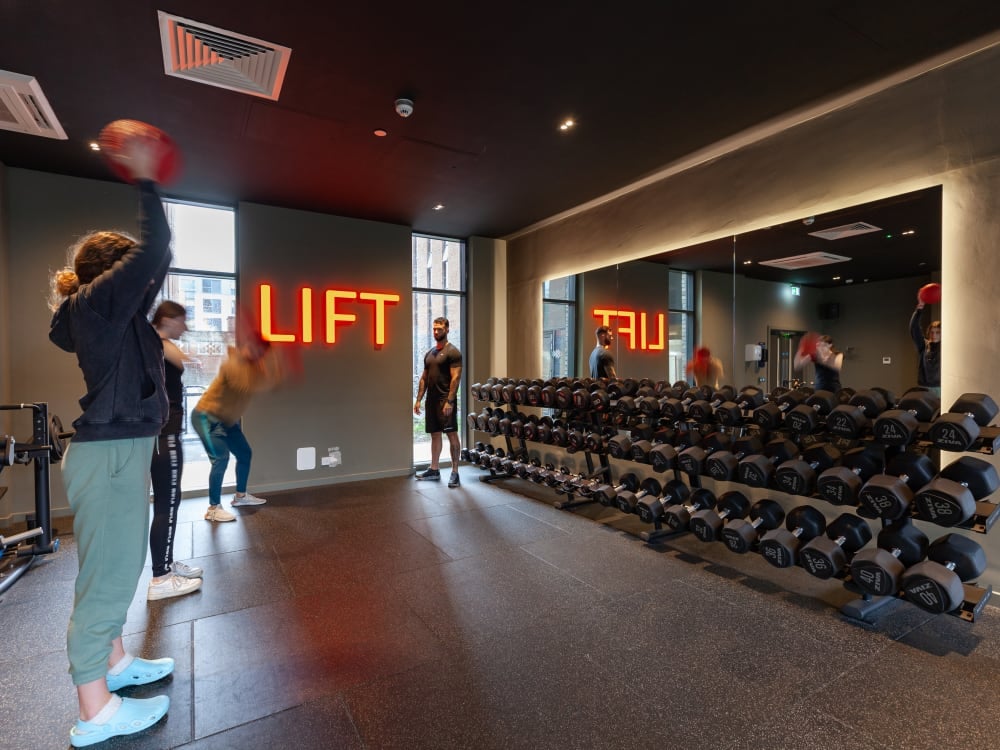 Students exercise near neon sign and dumbbells gym at True Liverpool in Liverpool Student Accommodation