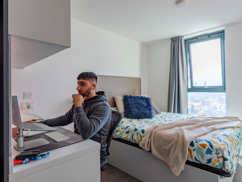 Man at desk with laptop next to bed bedroom at True Liverpool in Liverpool Student Accommodation