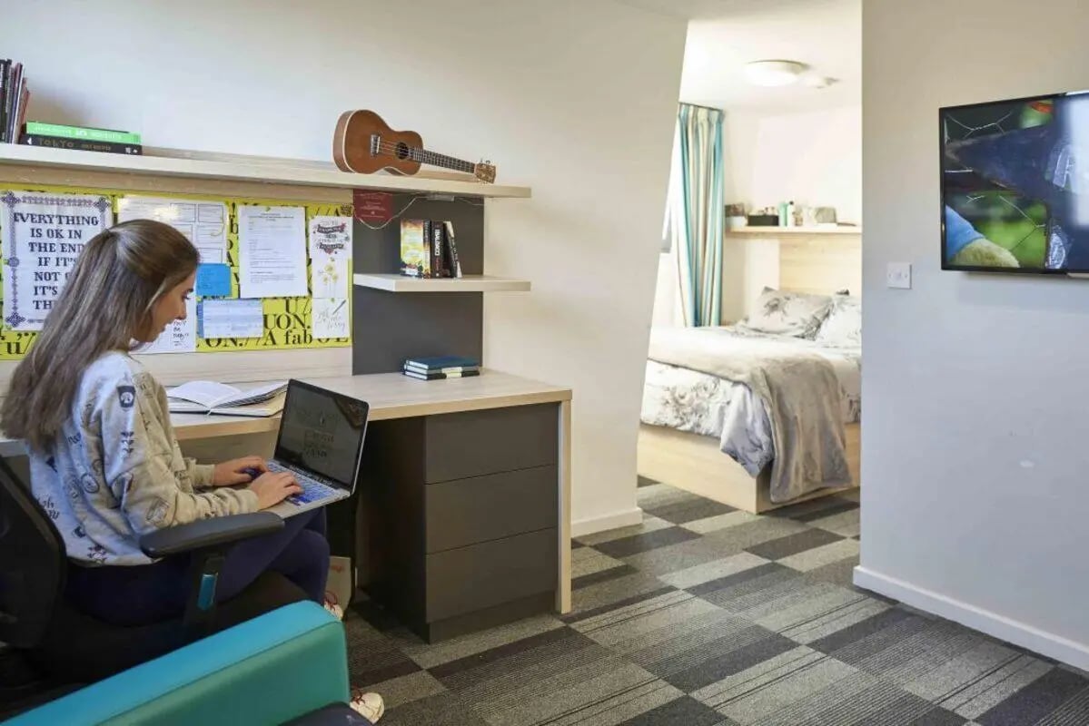 Student studying at desk with ukulele above bedroom study living room at The Railyard Cambridge in Cambridge Student Accommodation