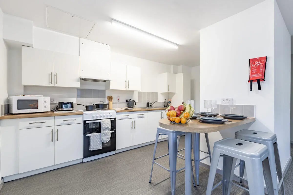 White cabinets stove microwave fruit bowl stools kitchen at Turner Court in Newcastle Upon Tyne Student Accommodation