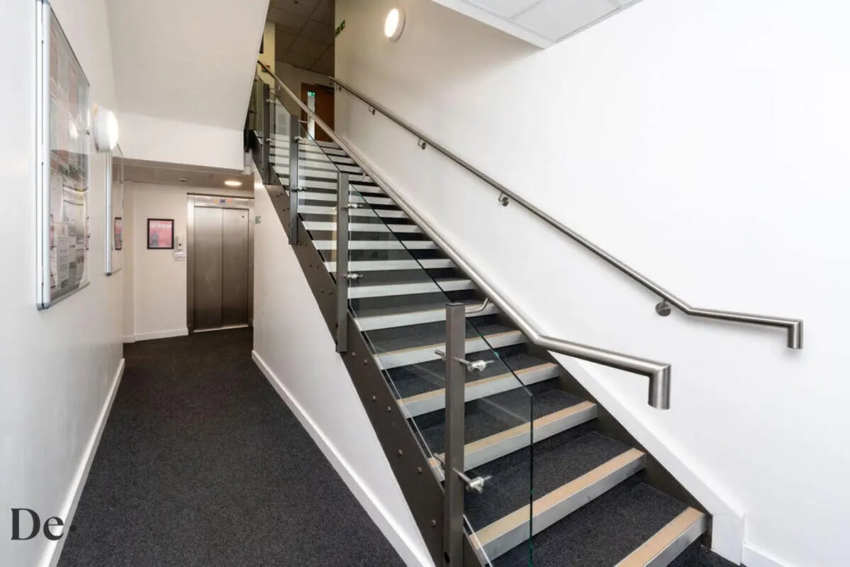 Modern staircase with glass panels and elevator lobby at Castle Hill in Cambridge Student Accommodation
