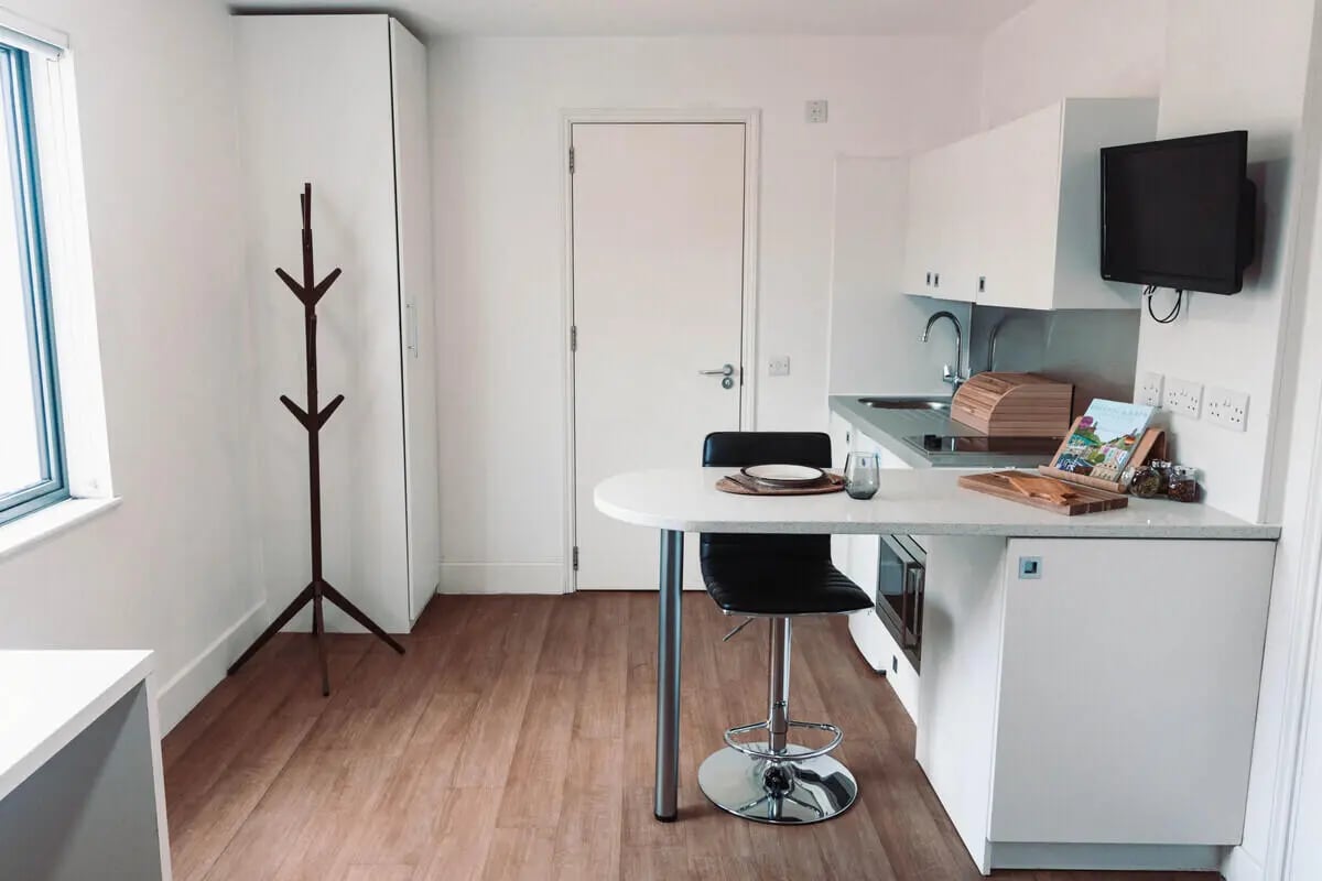 Coat rack table chair kitchen sink and TV kitchen area at Stonebridge House in Bristol Student Accommodation
