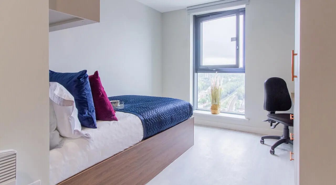 Bed with blue pillows chair by window bedroom at The Toybox in Birmingham Student Accommodation