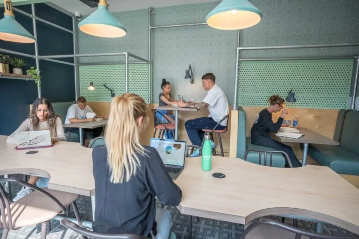 Students studying at tables with laptops and plants study area at The Toybox in Birmingham Student Accommodation