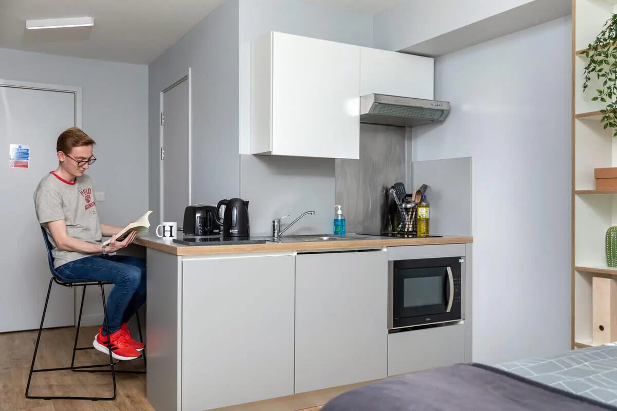Man reading at counter with kitchen appliances kitchen at The Depot in Bath Student Accommodation