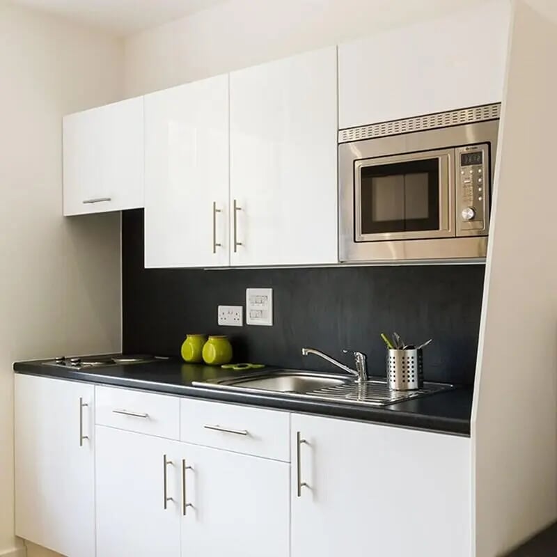 White cabinets microwave sink black countertop kitchen at The Courtyard Block C in Huddersfield Student Accommodation