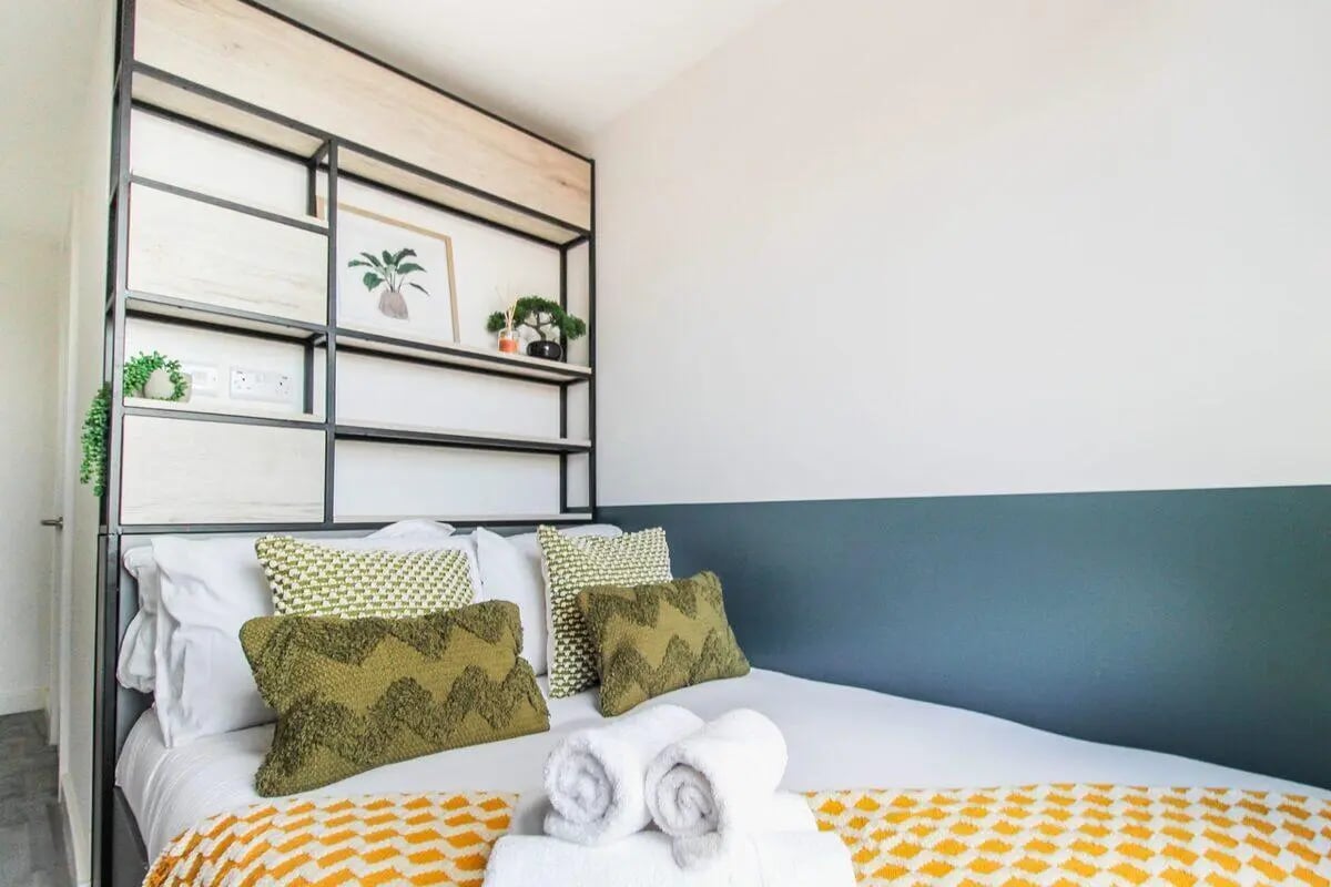 Bed with patterned pillows open shelves bedroom at The Nest Leicester in Leicester Student Accommodation