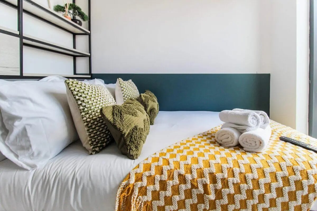 Bed with white linens decorative pillows yellow blanket bedroom at The Nest Leicester in Leicester Student Accommodation