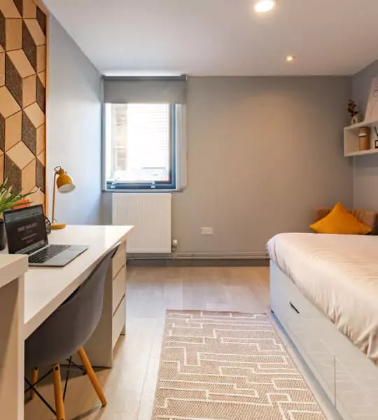 Desk laptop chair yellow lamp bed and rug bedroom at The Walls in Southampton Student Accommodation