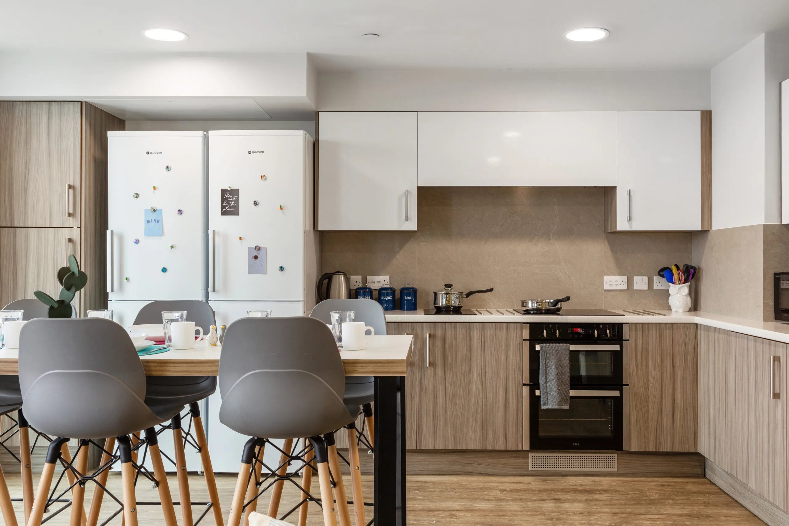 Two refrigerators table with chairs oven and cookware kitchen at Kaplan Living Brighton in Brighton Student Accommodation