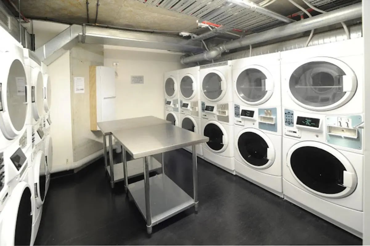 Row of white washing machines and stainless steel folding table laundry room at UniLodge Auckland City in Auckland Student Accommodation