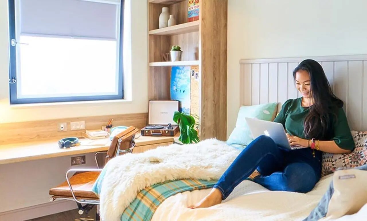 Woman on bed with laptop study desk Bedroom at Canvas The Parade in Cardiff Student Accommodation