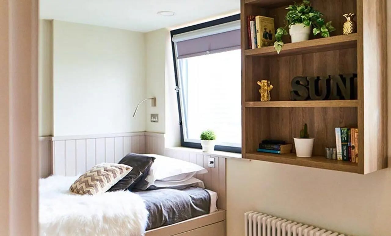Bed with fluffy throw bookshelf with plants books bedroom at Canvas The Parade in Cardiff Student Accommodation