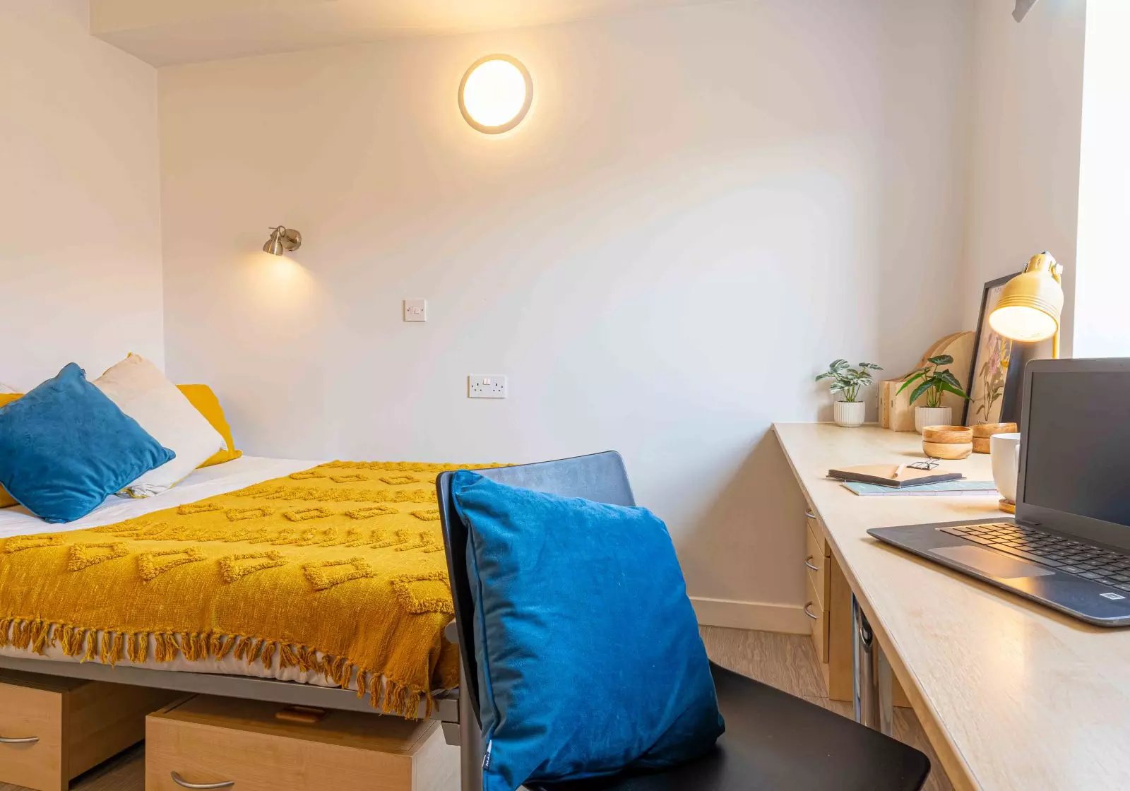 Bed with yellow blanket blue pillows desk with laptop Bedroom at iQ Arkwright House in Bradford Student Accommodation